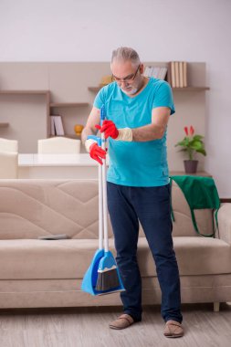 Yaşlı adam evi temizliyor.
