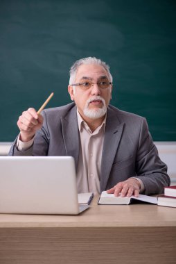 Tahtanın önünde yaşlı bir erkek öğretmen.