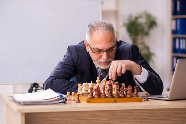 Viejo empleado jugando ajedrez en el lugar de trabajo — Foto de Stock