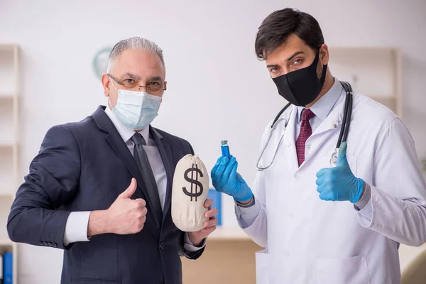 Old businessman visiting young male doctor in vaccination concep — Stock Photo, Image