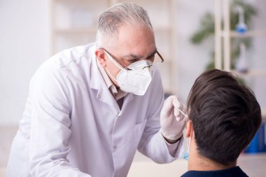 Genç erkek hasta salgın sırasında yaşlı erkek doktoru ziyaret ediyor.