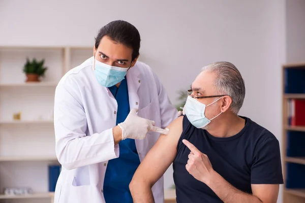 Старий відвідує молодого лікаря в концепції вакцинації ковадла-19 — стокове фото