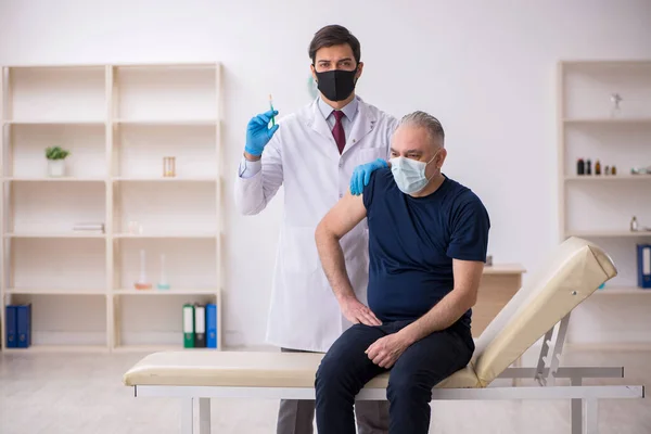 Old male patient visiting young male doctor in vaccination conce — Stock Photo, Image