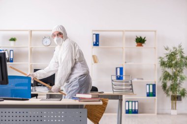 Yaşlı müteahhit elinde süpürgeyle ofisi temizliyor.