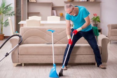 Yaşlı adam evi temizliyor.