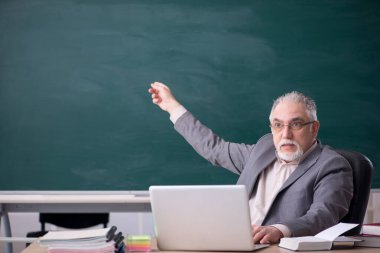 Tahtanın önünde yaşlı bir erkek öğretmen.