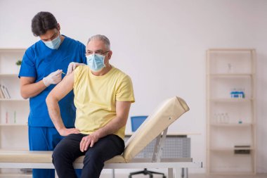 Yaşlı erkek hasta aşılama bölümünde genç bir erkek doktor.