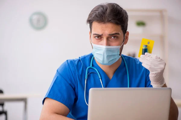 Young male doctor holding credit card during pandemic