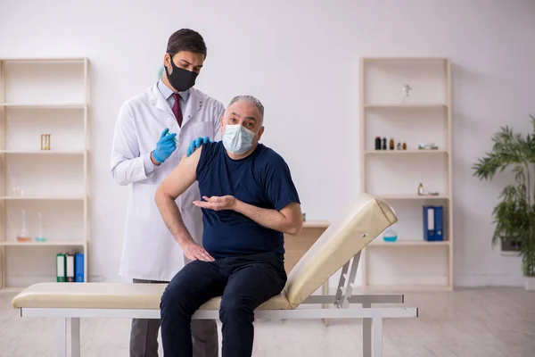 Vecchio paziente di sesso maschile in visita giovane medico di sesso maschile in conce vaccinazione — Foto Stock