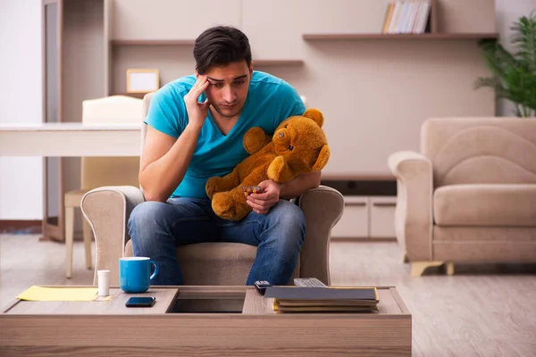 Jovem sentado com urso brinquedo em casa — Fotografia de Stock