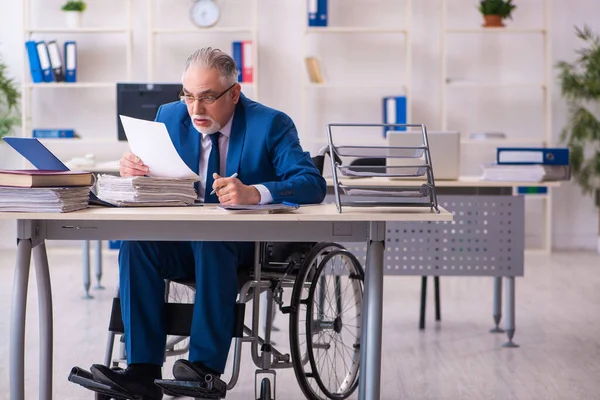 Oude mannelijke werknemer in rolstoel zittend op kantoor — Stockfoto