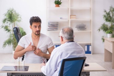 Genç erkek hasta yaşlı erkek doktoru ziyaret ediyor.