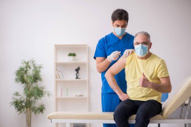 Yaşlı erkek hasta aşılama bölümünde genç bir erkek doktor.