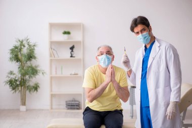 Yaşlı erkek hasta aşılama bölümünde genç bir erkek doktor.