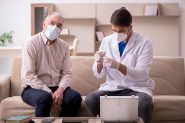 Genç erkek doktor aşı konseptinde yaşlı hastayı ziyaret ediyor.