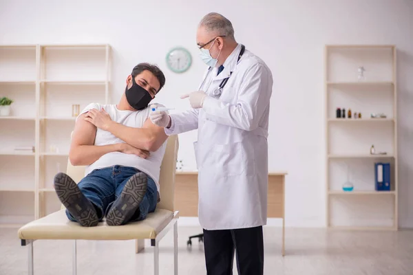 Mladý pacient mužského pohlaví navštěvující starého lékaře v vakcinačním konceptu — Stock fotografie