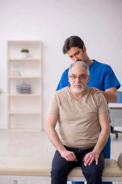 Vecchio maschio paziente visting giovane maschio medico chiropratico — Foto Stock