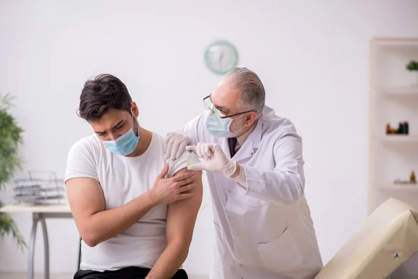 Молодий пацієнт, який відвідує старого лікаря під час вакцинації — стокове фото
