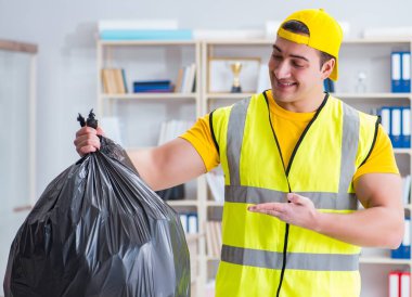 Ofisi temizleyen ve çöp torbası tutan bir adam.