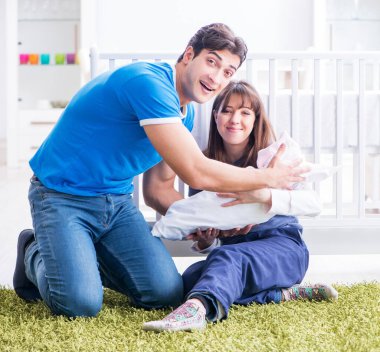 Yeni doğmuş bebekleriyle halıda oturan genç ebeveynler.