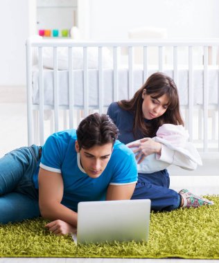 Yeni doğmuş bebekleriyle halıda oturan genç ebeveynler.