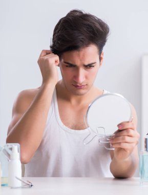 Genç yakışıklı adam aynaya bakıyor.