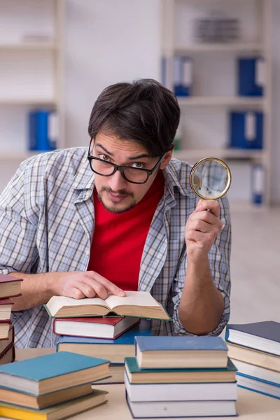 Ung manlig elev och för många böcker i klassrummet — Stockfoto