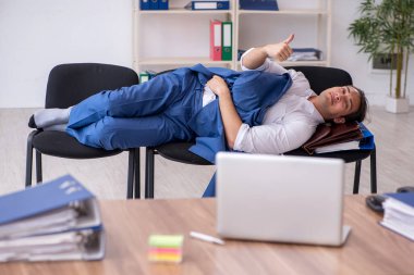 Genç bir erkek çalışan ofiste koltuklarda uyuyor.