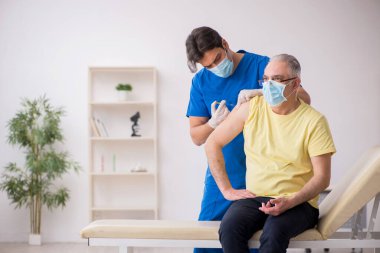Yaşlı erkek hasta aşılama bölümünde genç bir erkek doktor.