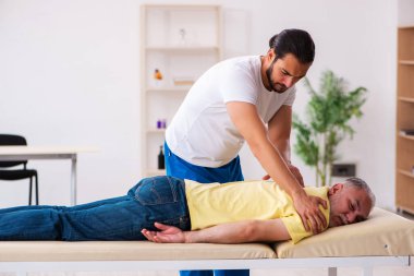 Yaşlı erkek hasta, genç erkek doktor masörünü ziyaret ediyor.