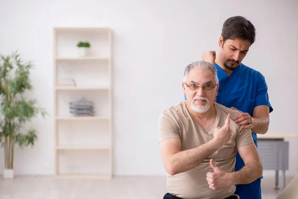 Old male patient visting young male doctor chiropractor — Stock Photo, Image