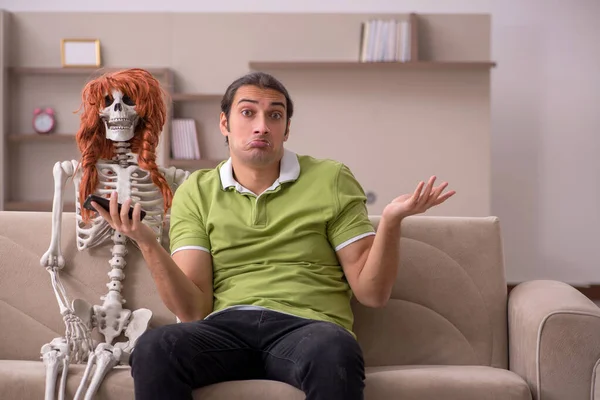 Молодой человек сидит на диване с женским скелетом — стоковое фото