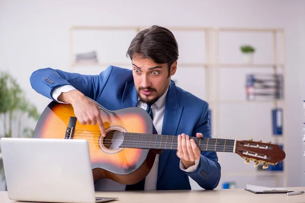 Joven empleado masculino tocando guitarra en el lugar de trabajo —  Fotos de Stock