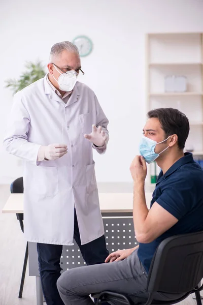 Jovem paciente do sexo masculino visitando velho médico masculino durante a pandemia — Fotografia de Stock