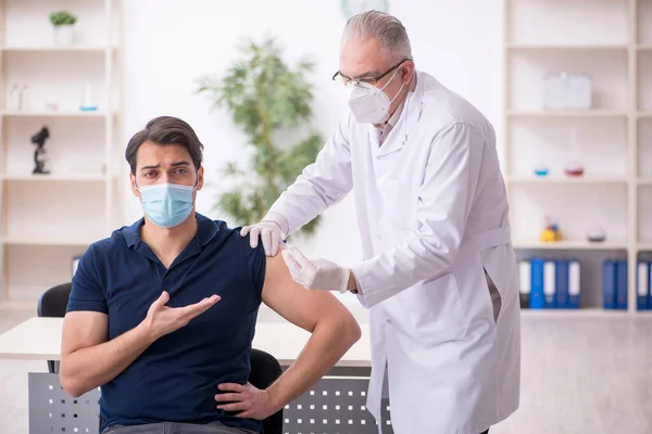 Mladý mužský pacient na návštěvě starého mužského lékaře ve vakcinaci conce — Stock fotografie