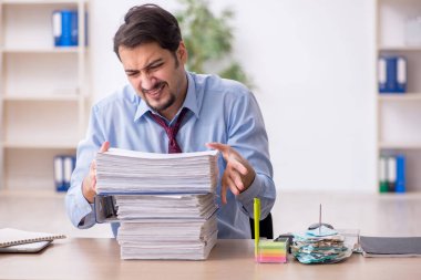 Genç bir erkek çalışan ve ofiste çok fazla iş var.