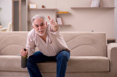 Yaşlı adam evde alkol içiyor.