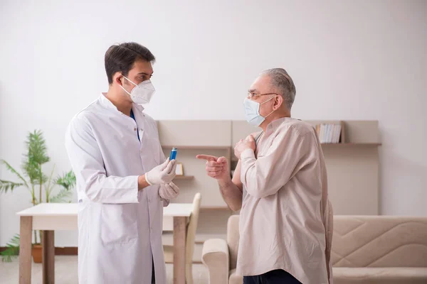 Mladý lékař mužského pohlaví navštíví starého pacienta ve vakcinačním konceptu — Stock fotografie
