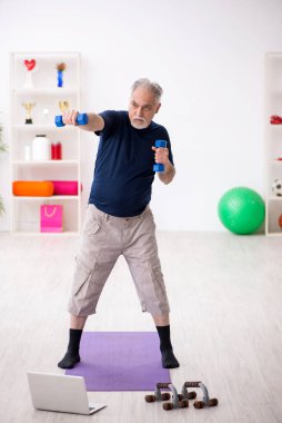 Yaşlı adam içeride spor egzersizleri yapıyor.