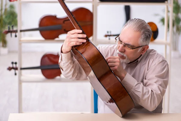 Viejo reparador masculino reparando instrumentos musicales en el lugar de trabajo — Foto de Stock