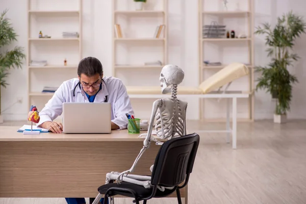 Молодой врач и пациент со скелетом в клинике — стоковое фото