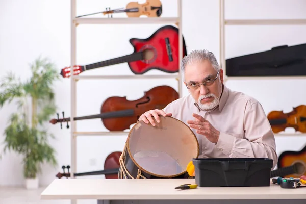 Old male repairman repairing musical instruments at workplace — Stock Photo, Image
