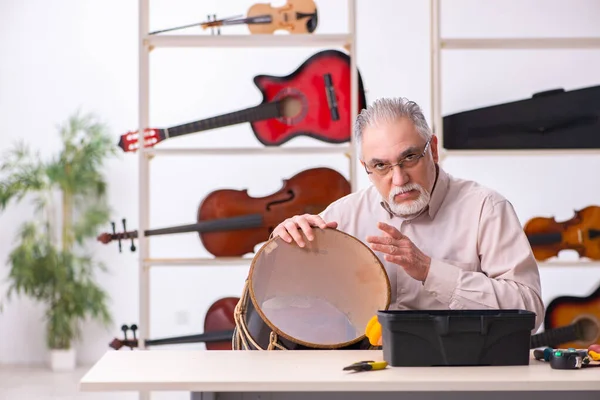 Oude mannelijke reparateur repareert muziekinstrumenten op het werk — Stockfoto