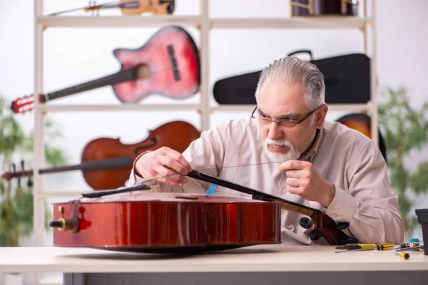 Oude mannelijke reparateur repareert muziekinstrumenten op het werk — Stockfoto