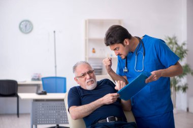 Yaşlı adam genç erkek doktoru ziyaret ediyor.