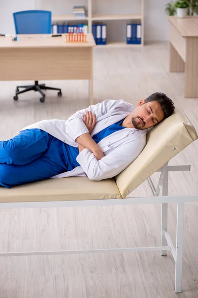Κουρασμένος νεαρός άνδρας γιατρός ξαπλωμένος στον καναπέ του νοσοκομείου — Φωτογραφία Αρχείου