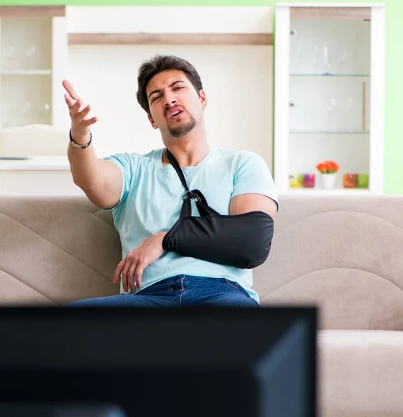 Braço ferido homem sentado no sofá assistindo tv — Fotografia de Stock