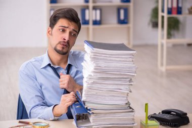 Genç bir erkek çalışan ve ofiste çok fazla iş var.