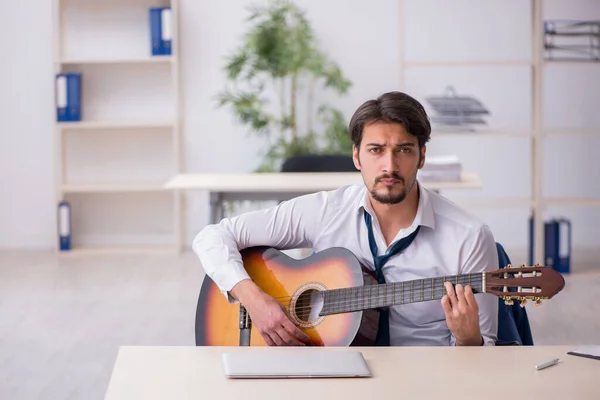 Jovem funcionário do sexo masculino tocando guitarra no local de trabalho — Fotografia de Stock