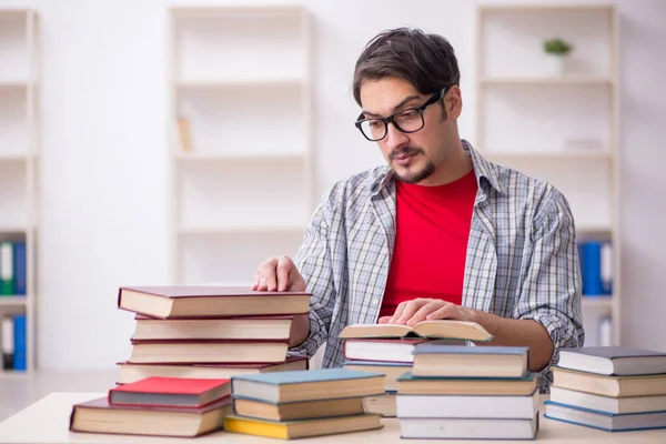 Jovem estudante do sexo masculino e muitos livros em sala de aula — Fotografia de Stock